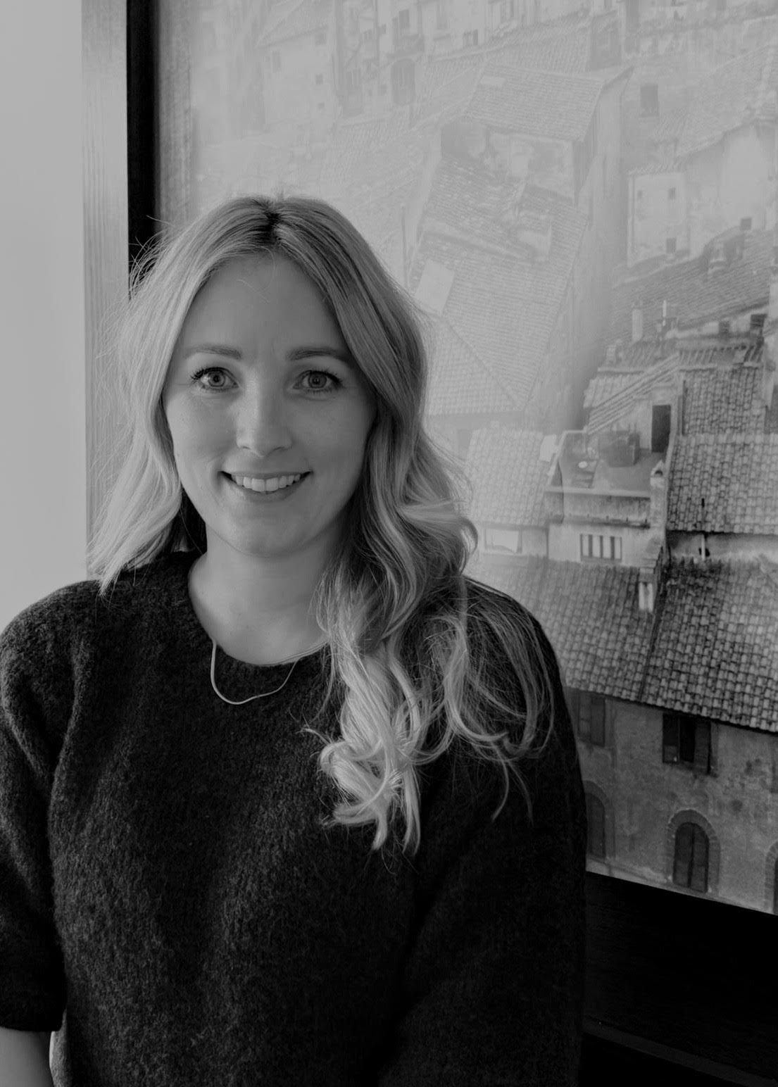 Auf einem Schwarzweißfoto mit einer Stadt im Hintergrund lächelt eine Frau.