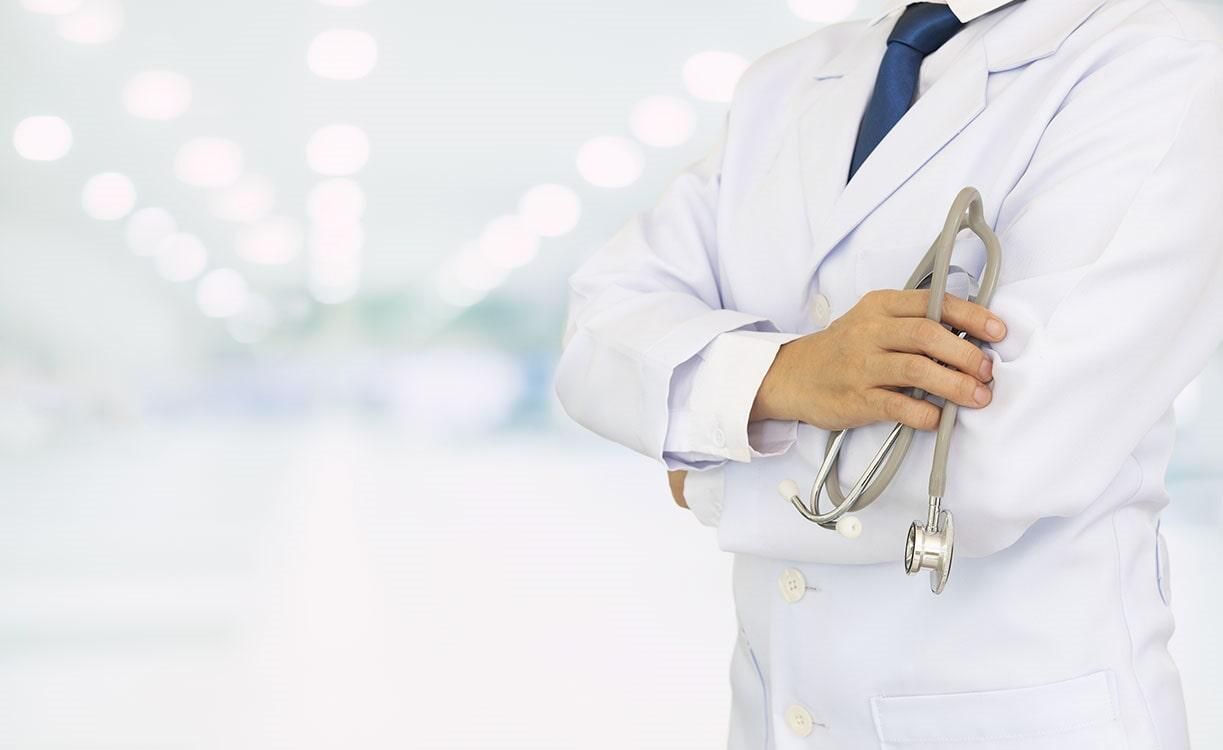Un médico con bata blanca y corbata sostiene un estetoscopio.