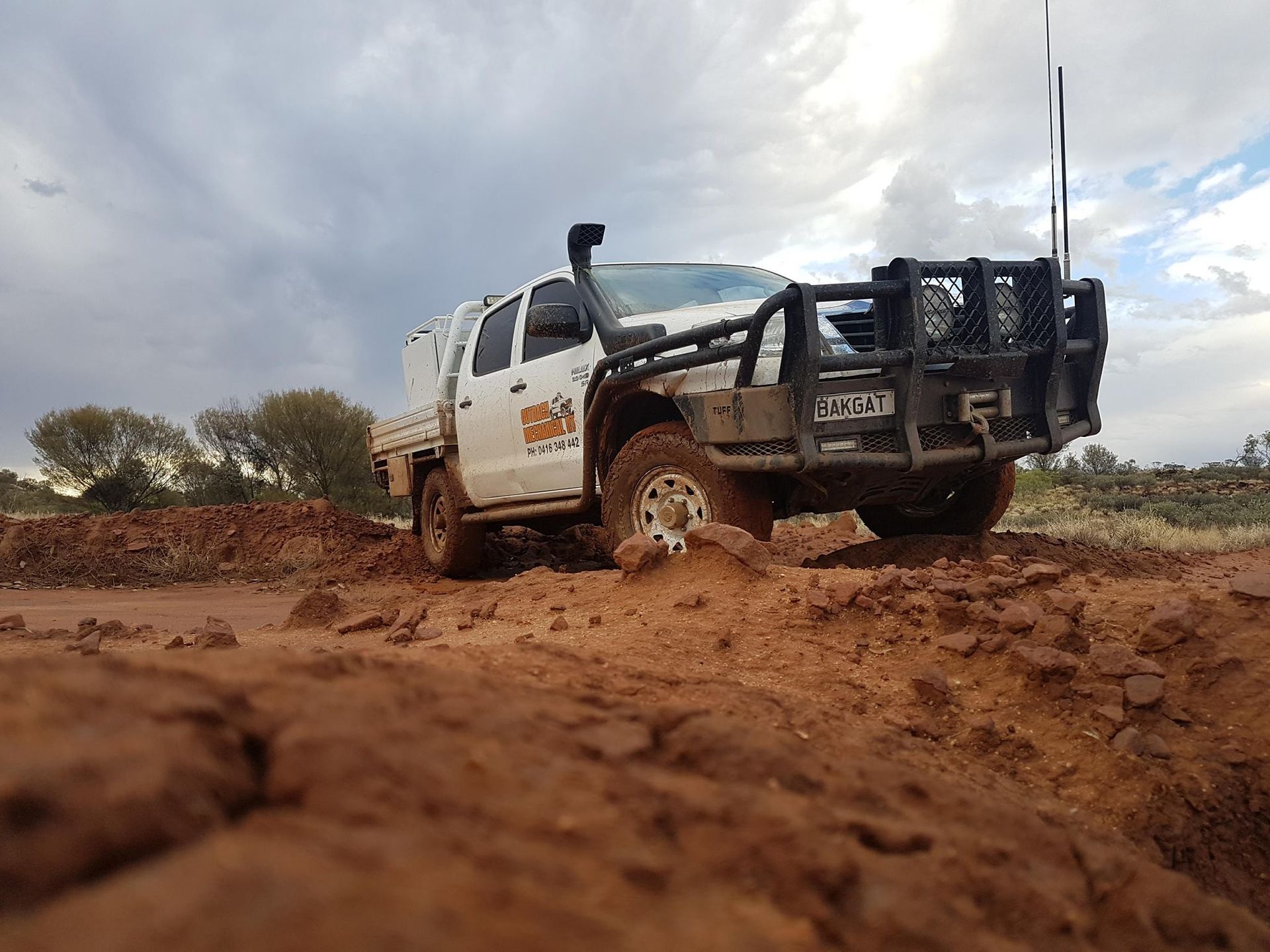 A White Truck Is Driving Through A Muddy Dirt Road — Red Central Towing & Recovery In Alice Springs, NT