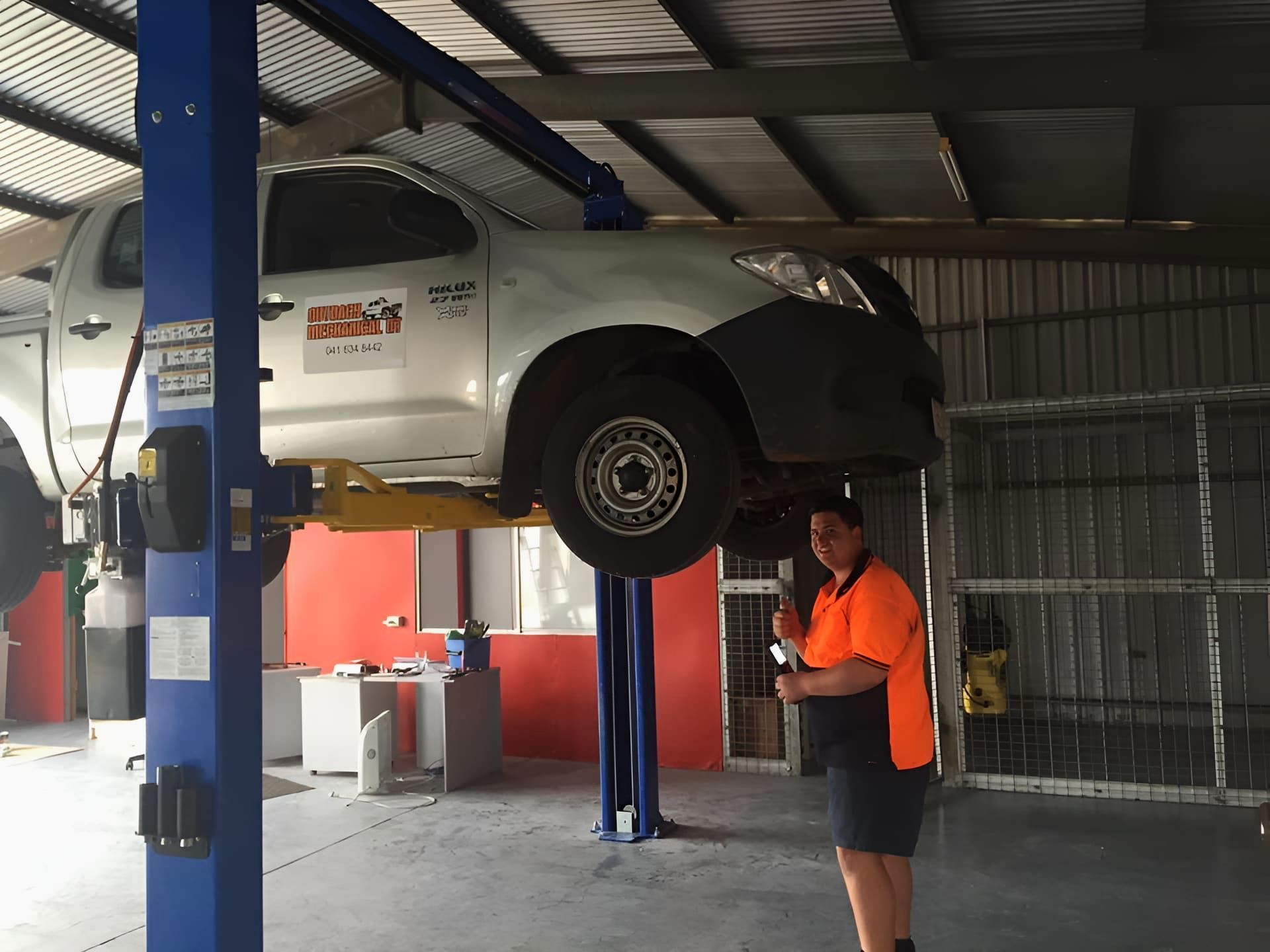 A Man Is Standing Next To A Truck On A Lift In A Garage — Red Central Towing & Recovery In Alice Springs, NT