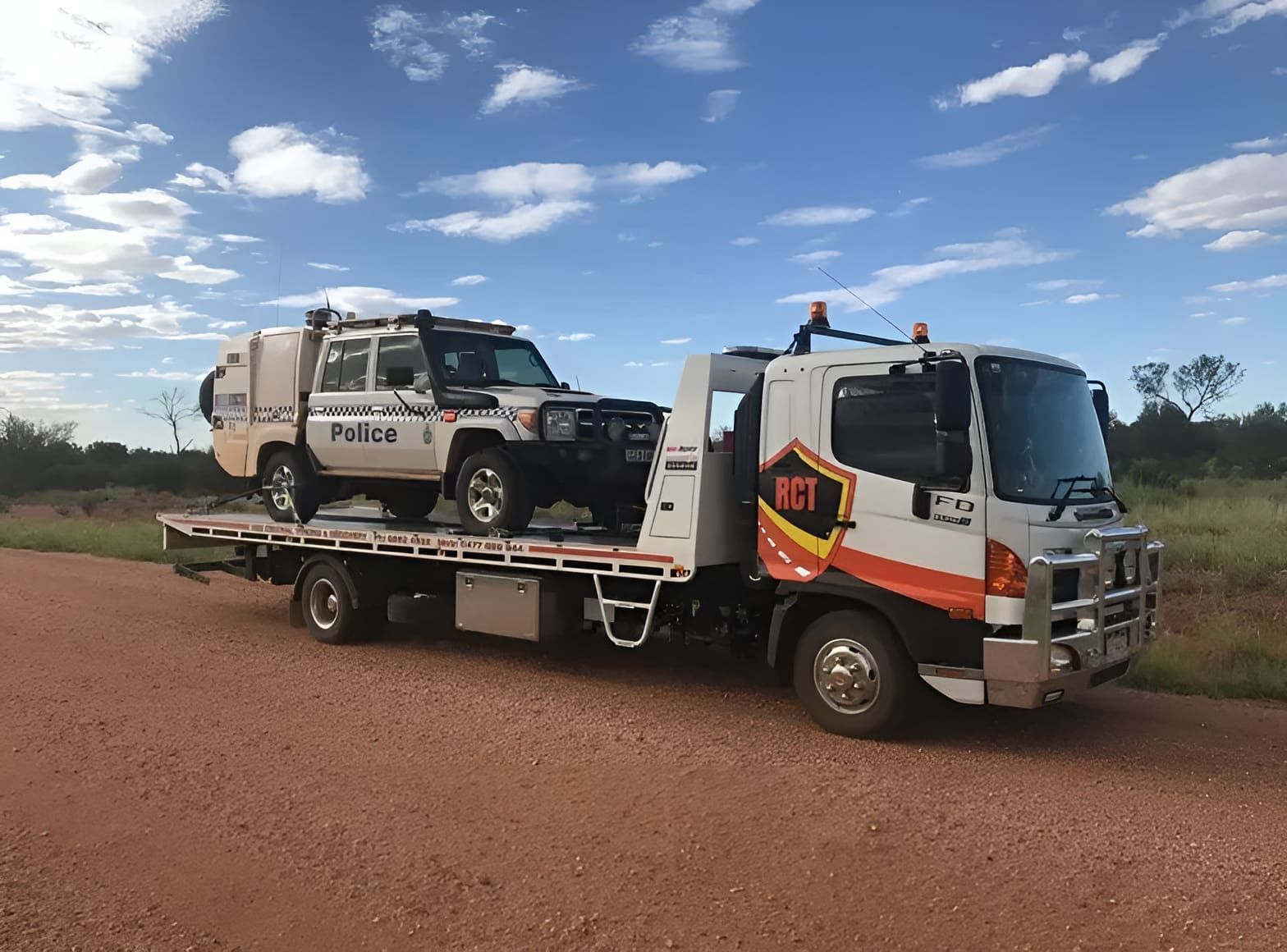 A Tow Truck Is Carrying Two Cars On A Dirt Road — Red Central Towing & Recovery In Alice Springs, NT
