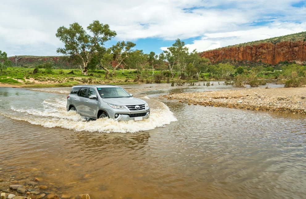 A Car is Driving Through a River on a Dirt Road — Red Central Towing & Recovery In Alice Springs, N