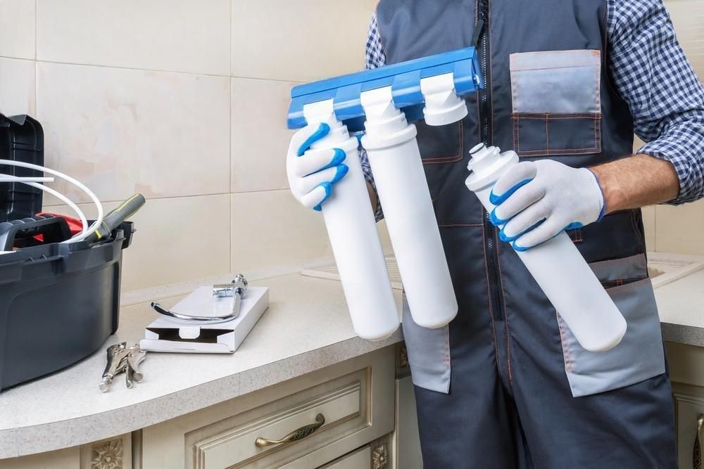 A man is holding two water filters in his hands in a kitchen.