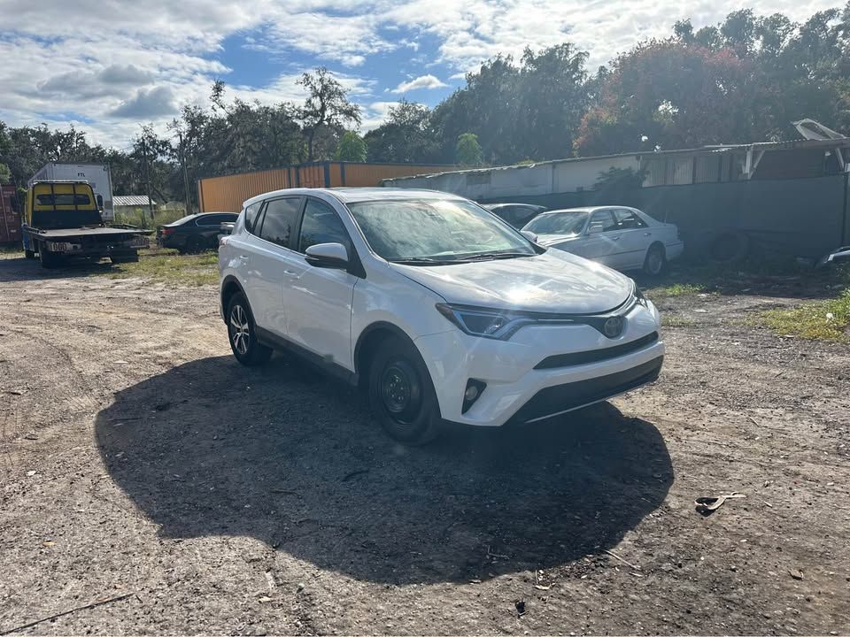 White Toyota RAV4 parked on gravel; tow truck and other cars in background.