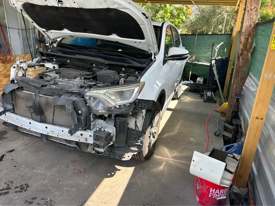 White SUV with front-end damage, hood open, parked in a garage.