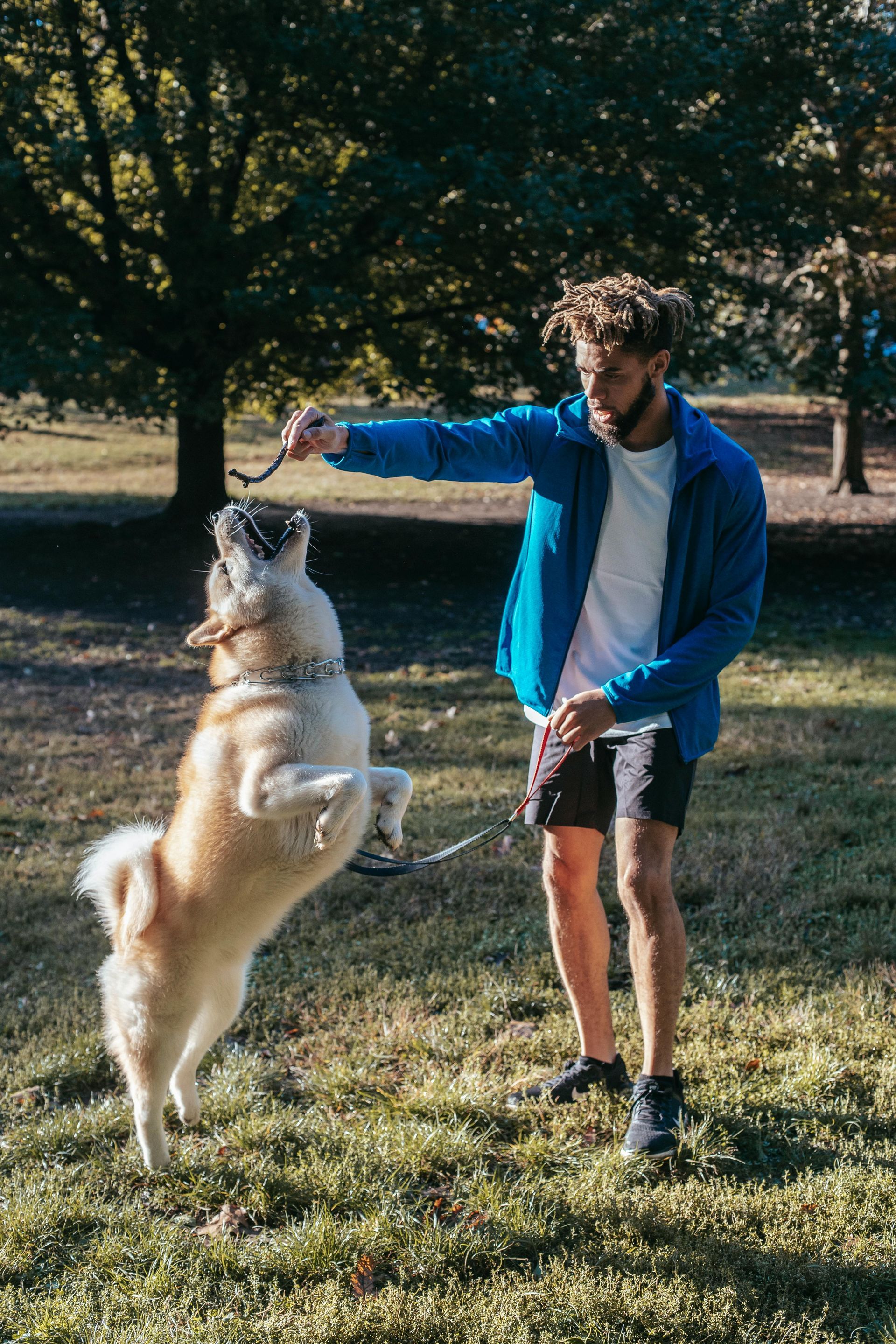 A woman is standing next to a puppy that is running in the grass.