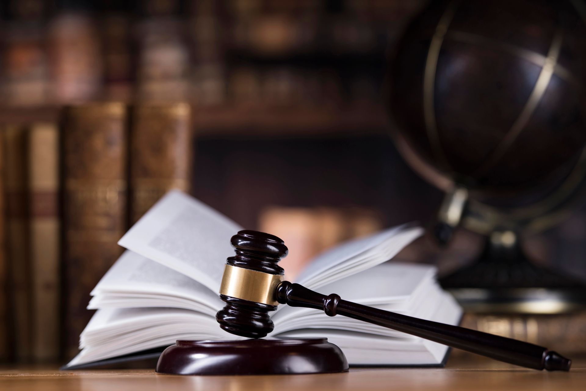 Martelletto su un libro di diritto aperto, con un mappamondo e dei libri sullo sfondo.