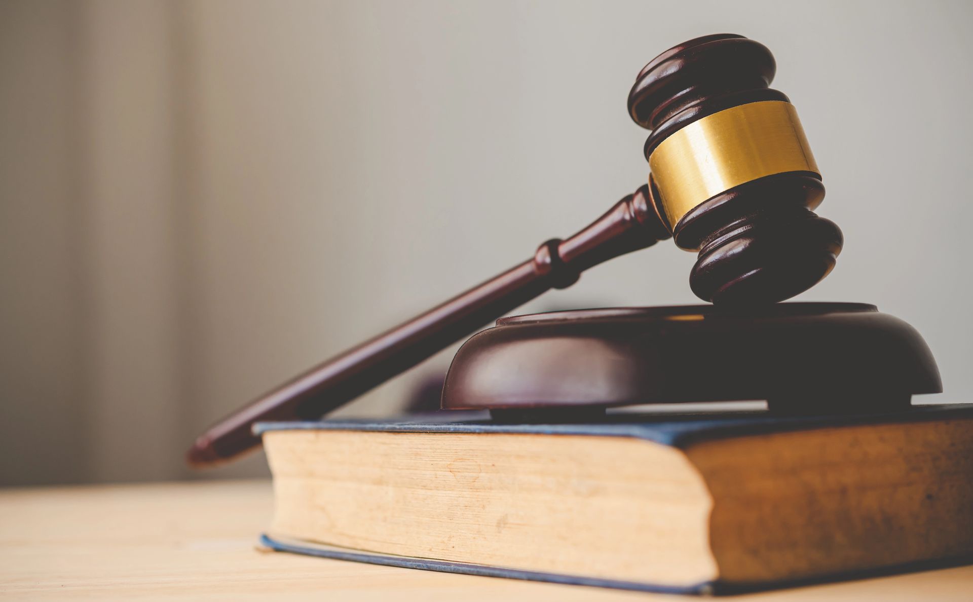 Martelletto di legno con fascia dorata appoggiato su un libro di leggi.