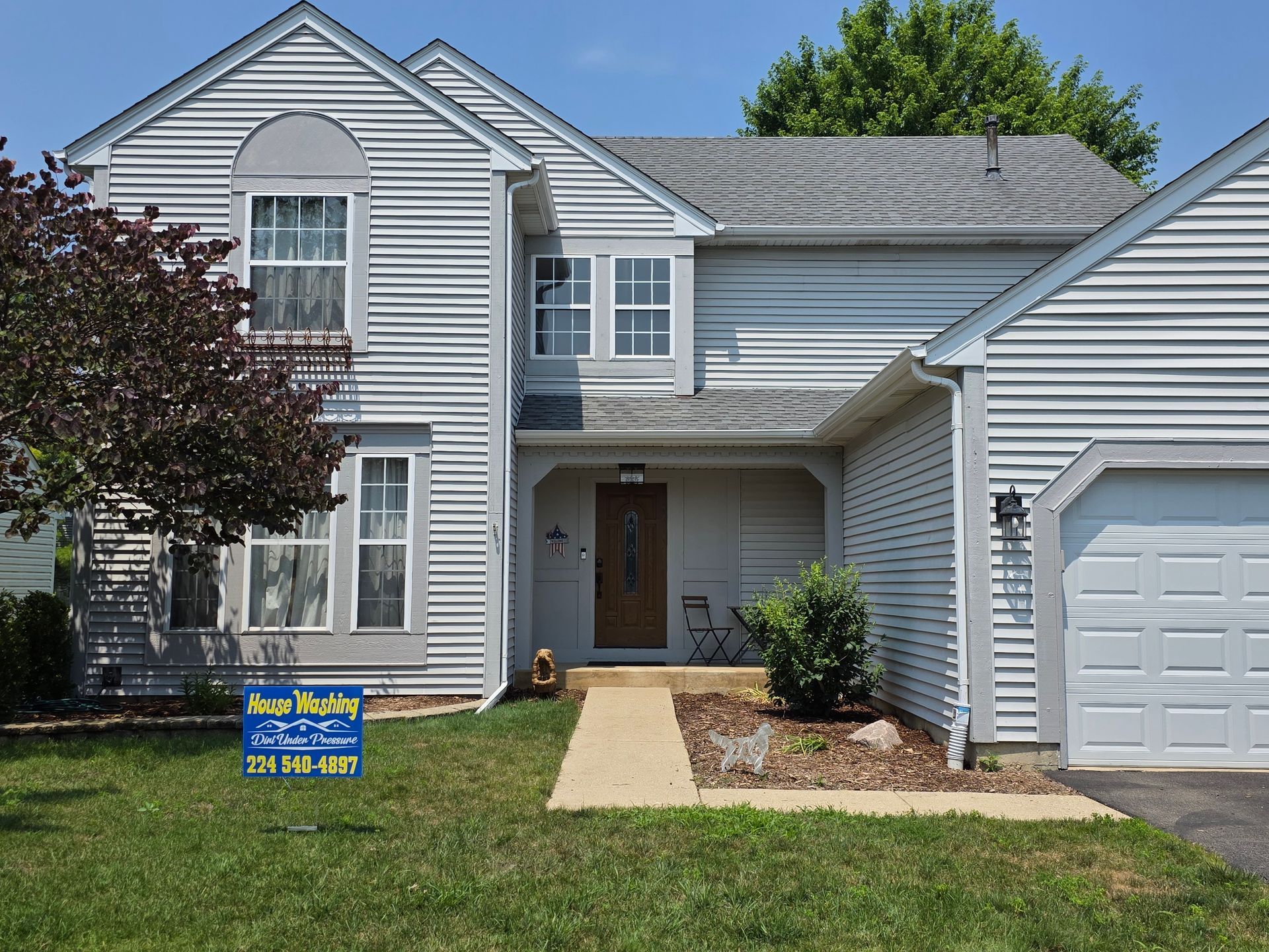 Two-story gray house with a brown door and garage. Blue for sale sign on the front lawn.