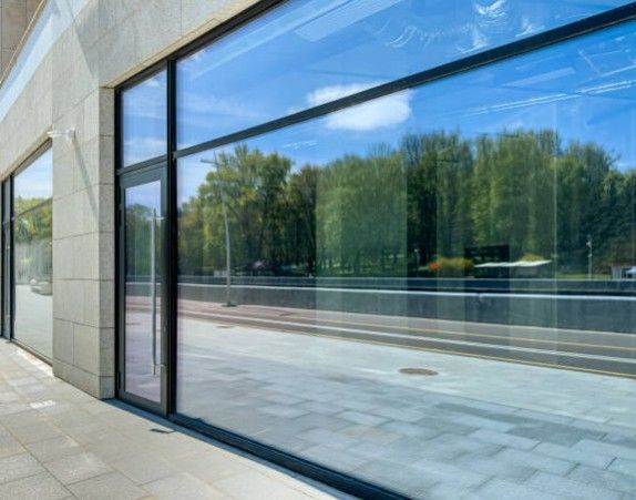 Large glass windows reflecting a sunny day with trees and a sky.