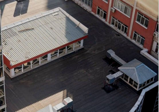 Rooftop view of buildings with flat roofs. One has a metal roof with red trim, others are flat and black.
