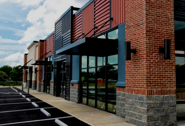 Row of retail storefronts with red, black, and gray exteriors; parking lot in the foreground.
