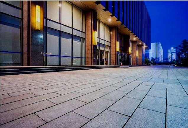 Exterior of a modern building with a tiled plaza at dusk. Blue and gold lighting.