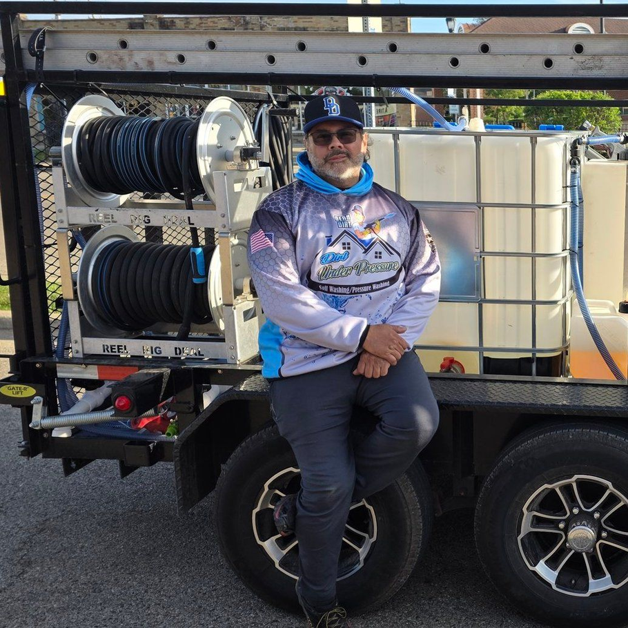 Man leaning against a trailer with water tanks, wearing a blue and white logo shirt and hat.
