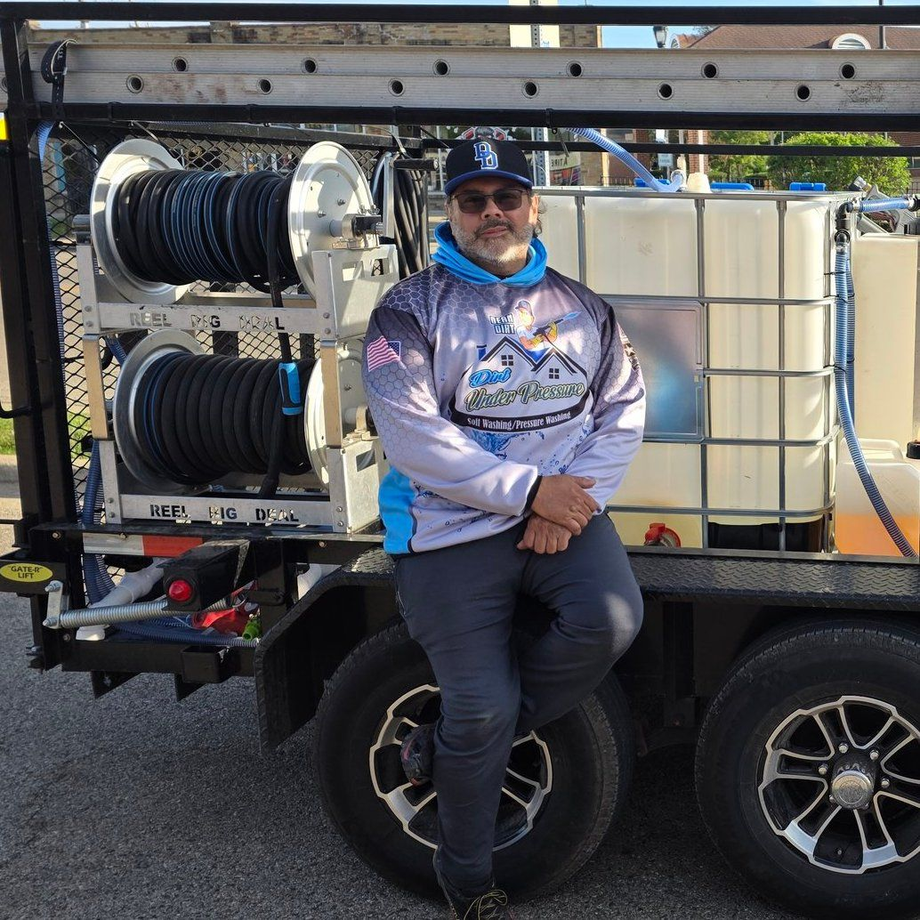 Man in front of mobile cleaning unit. He's wearing a hoodie, leaning on a tire, outdoors.