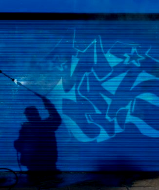A person power washing graffiti from a blue metal garage door.