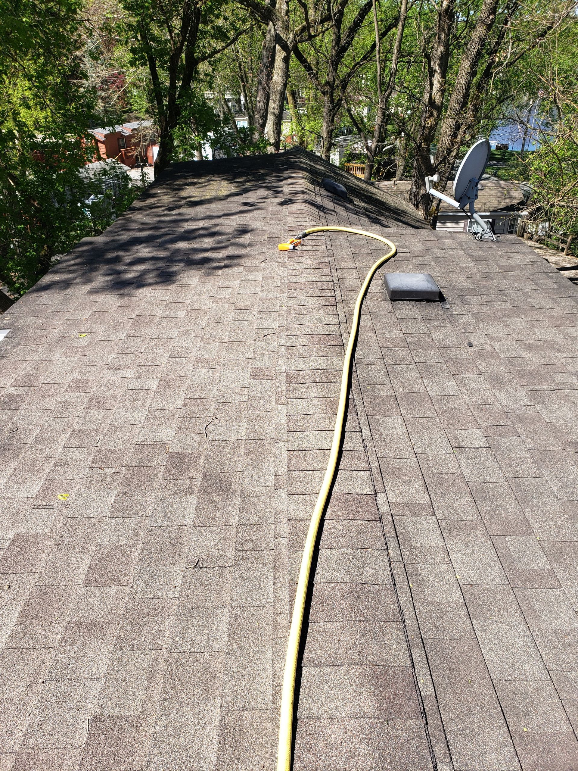 Brown roof with a yellow hose leading from the bottom to the top, surrounded by green trees.