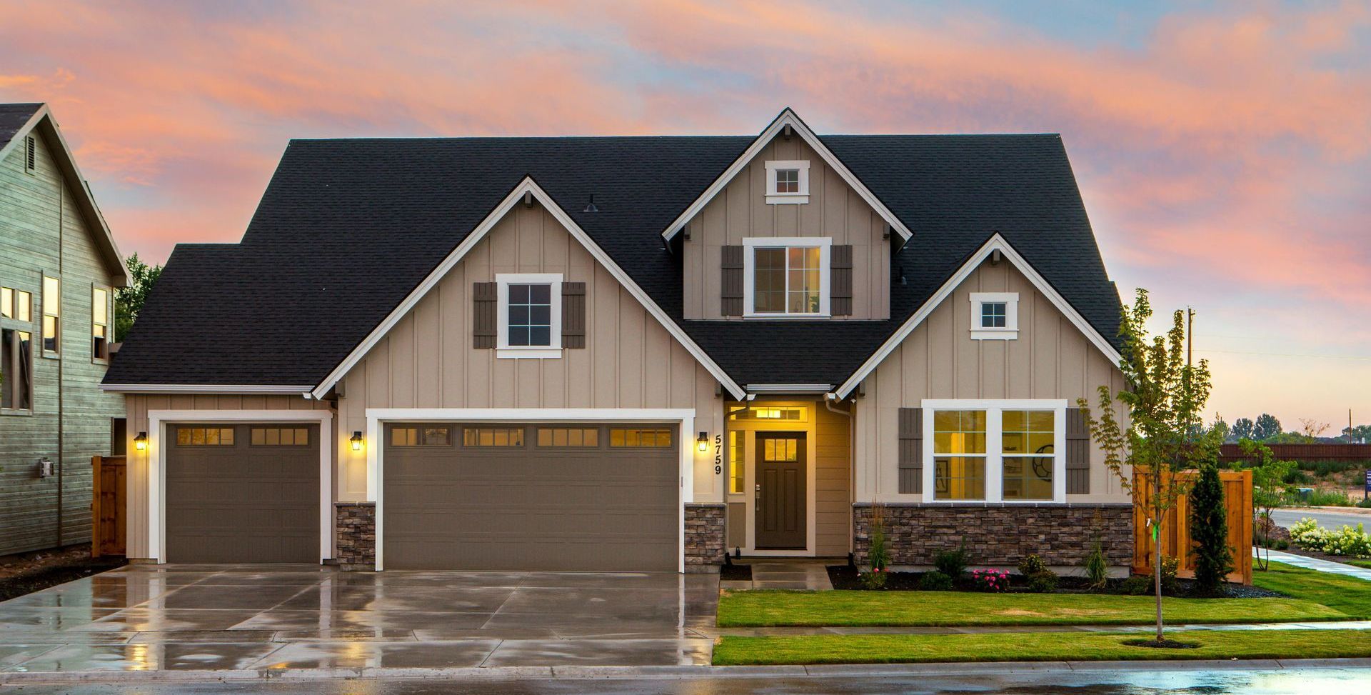 Tan house with black roof, two-car garage, and lawn. Sunset sky.