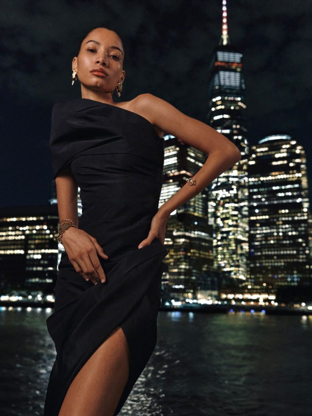 Una mujer con un vestido blanco y negro está parada en un muro de piedra.