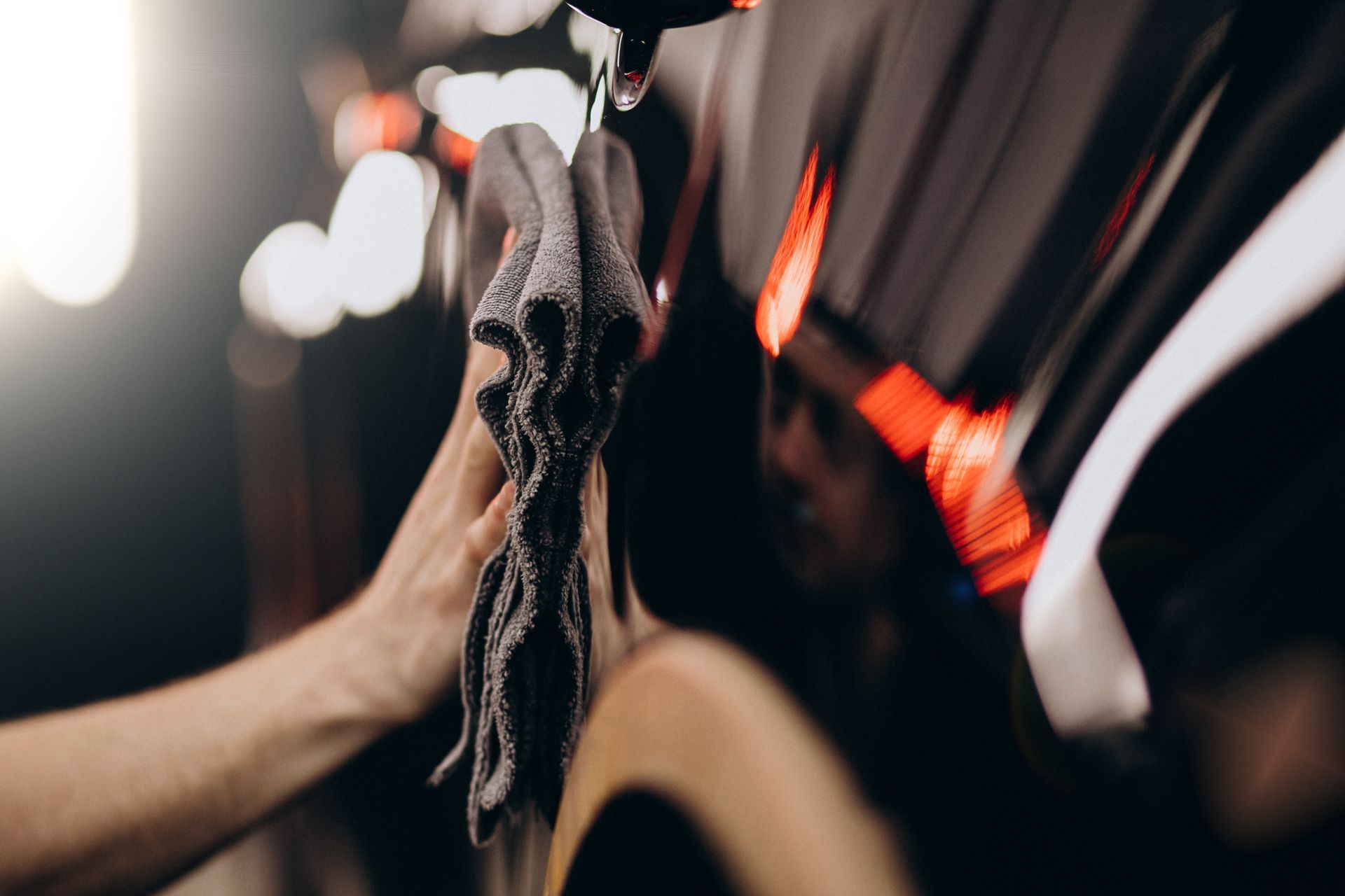 A person’s hand using a grey microfiber cloth to clean a smooth, dark surface under bright lighting.
