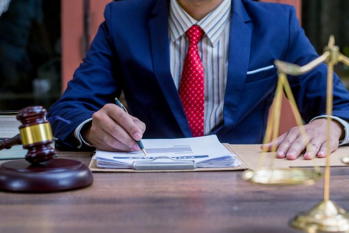 A man in a suit and tie is sitting at a table writing on a clipboard.