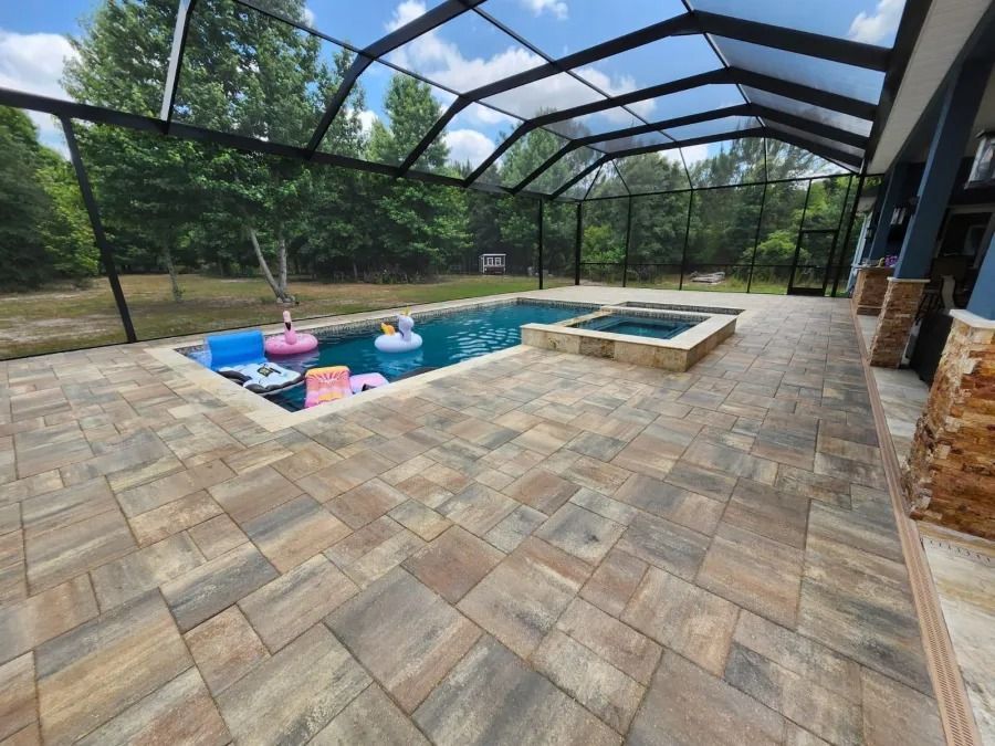 Pool patio with pool, hot tub, and screened enclosure. Paver patio in light brown and gray colors.