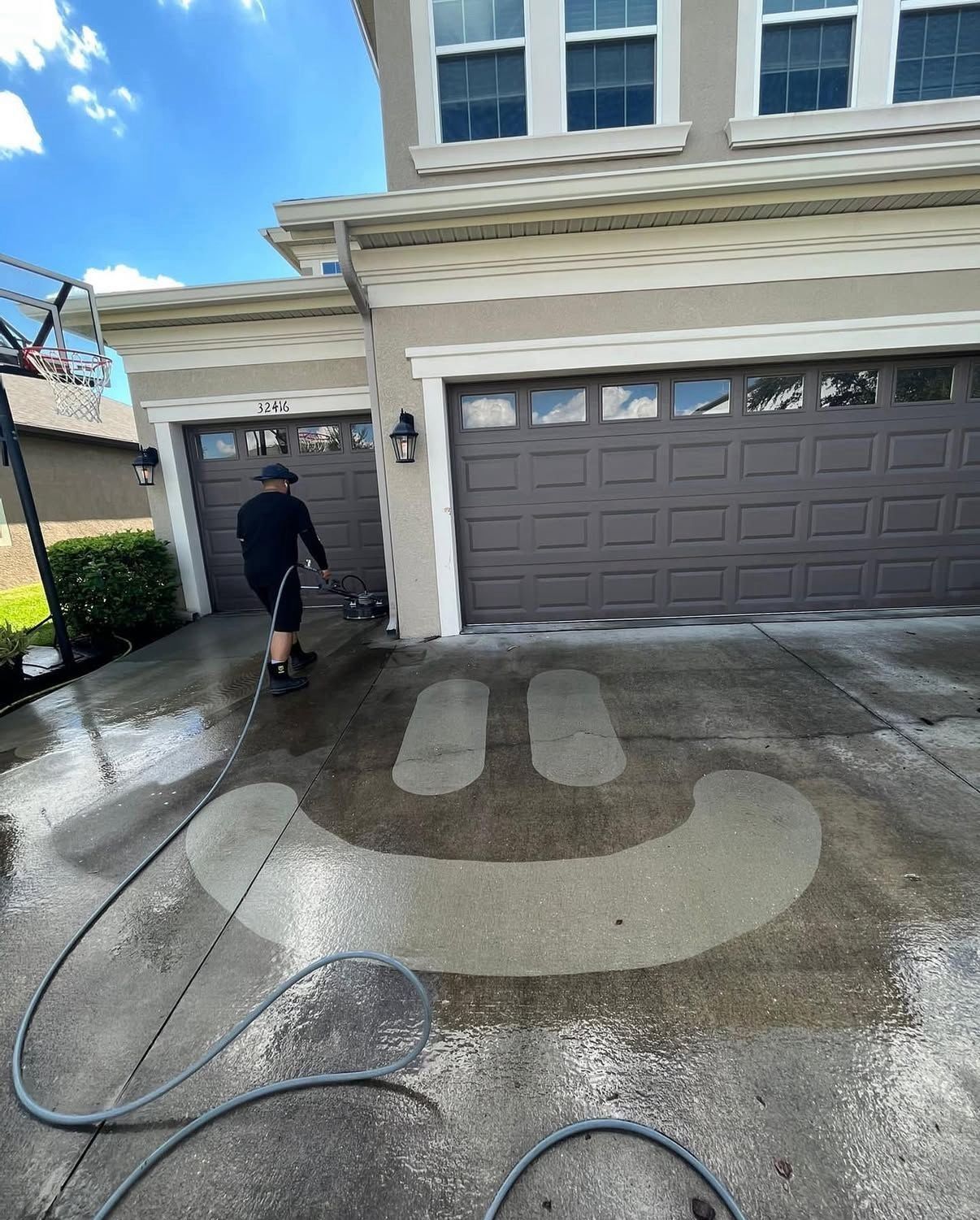 Person power washing a smiley face onto a driveway in front of a house.