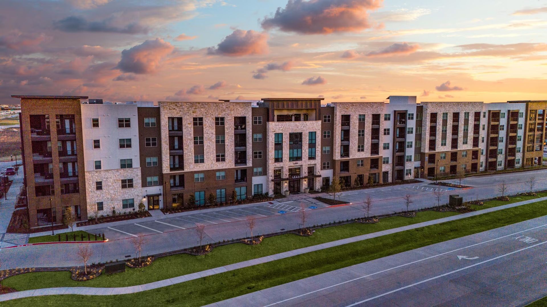 Modern apartment complex at sunset with a road and grassy median in front