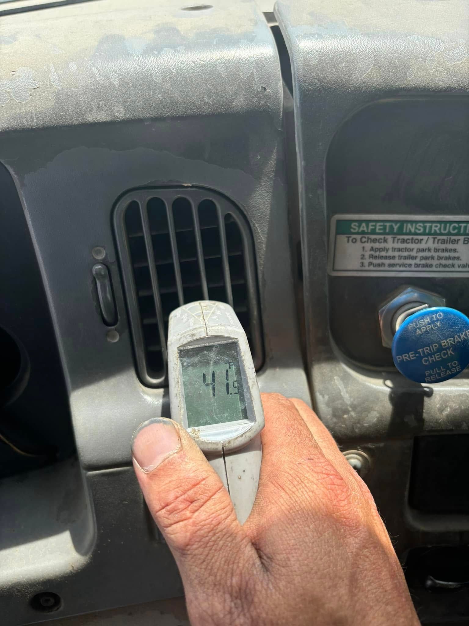 A hand holds an infrared thermometer displaying a temperature of 41 degrees in front of a vehicle's air conditioning vent.