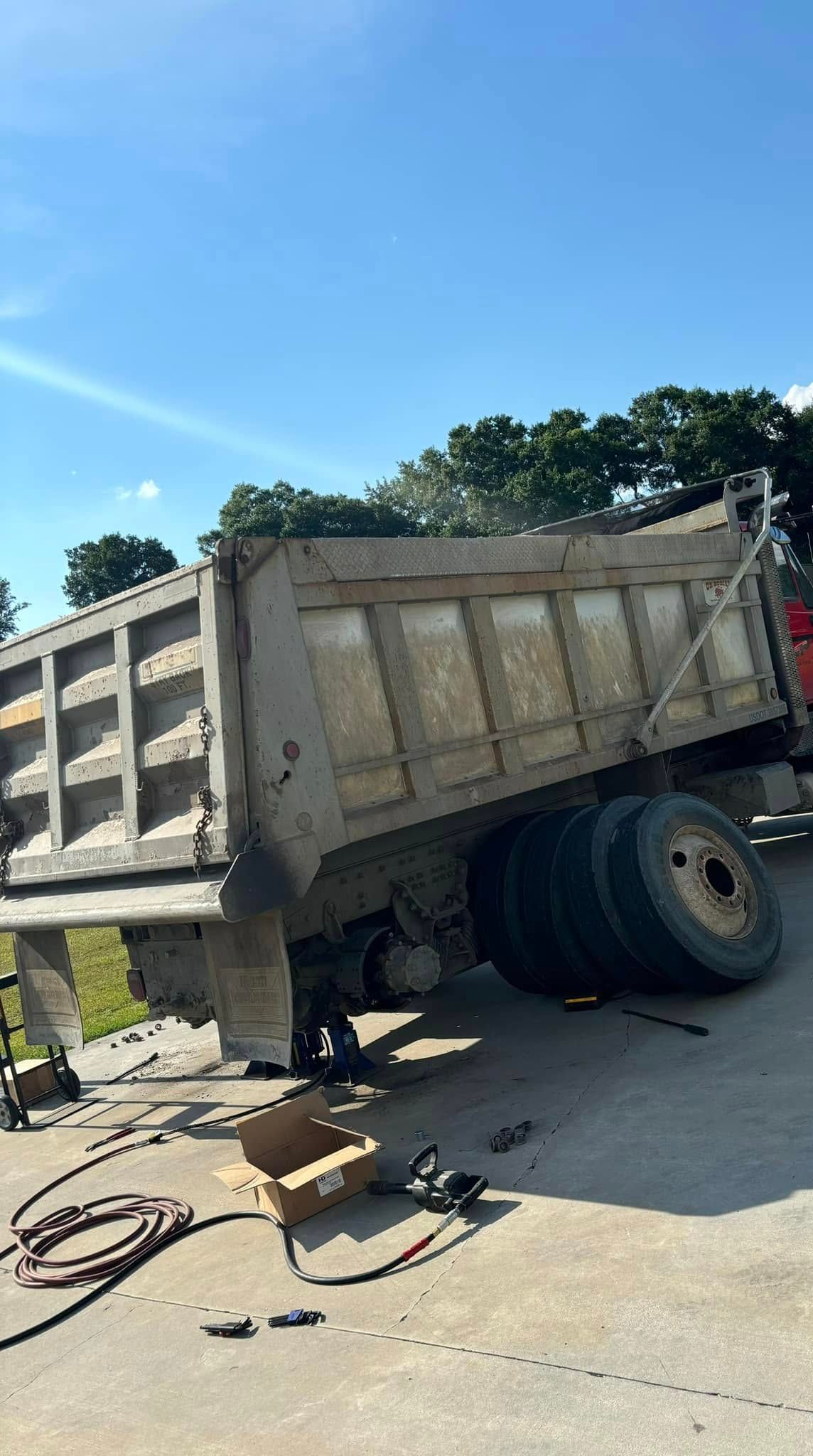 A dump truck body is propped up by a jack on a concrete surface, with loose tires and tools nearby.