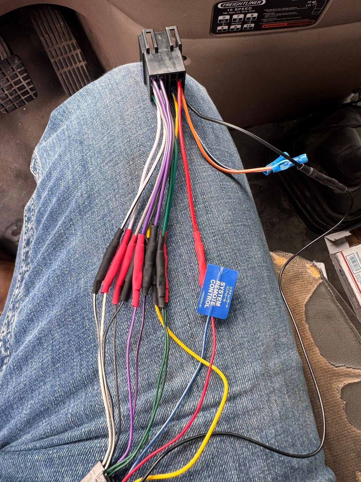 A multi-colored car stereo wiring harness with spliced and crimped wires, resting on a person's blue denim-clad lap.