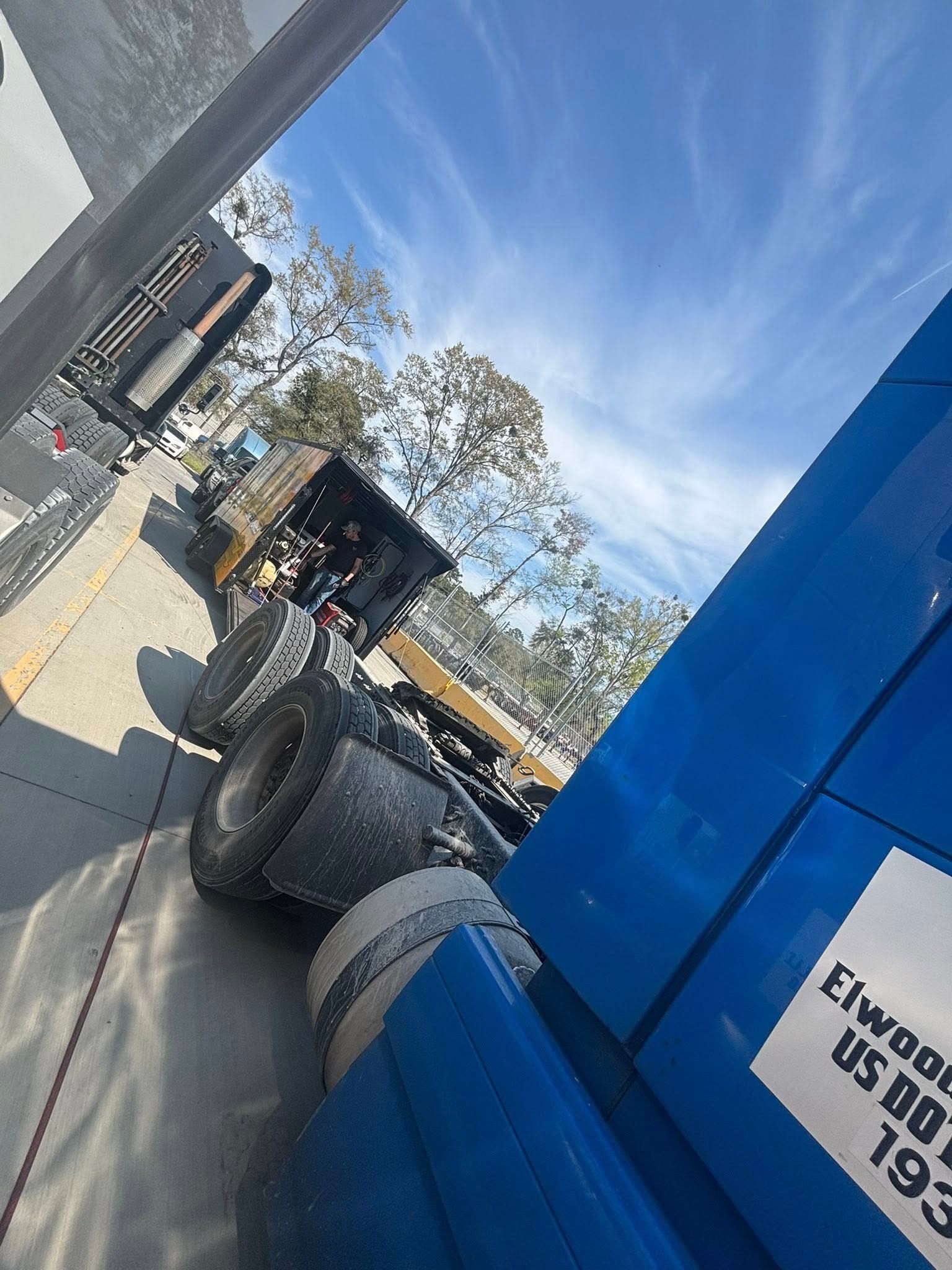 A close-up view of the rear wheels and frame of a blue semi-truck parked outdoors under a bright blue sky.