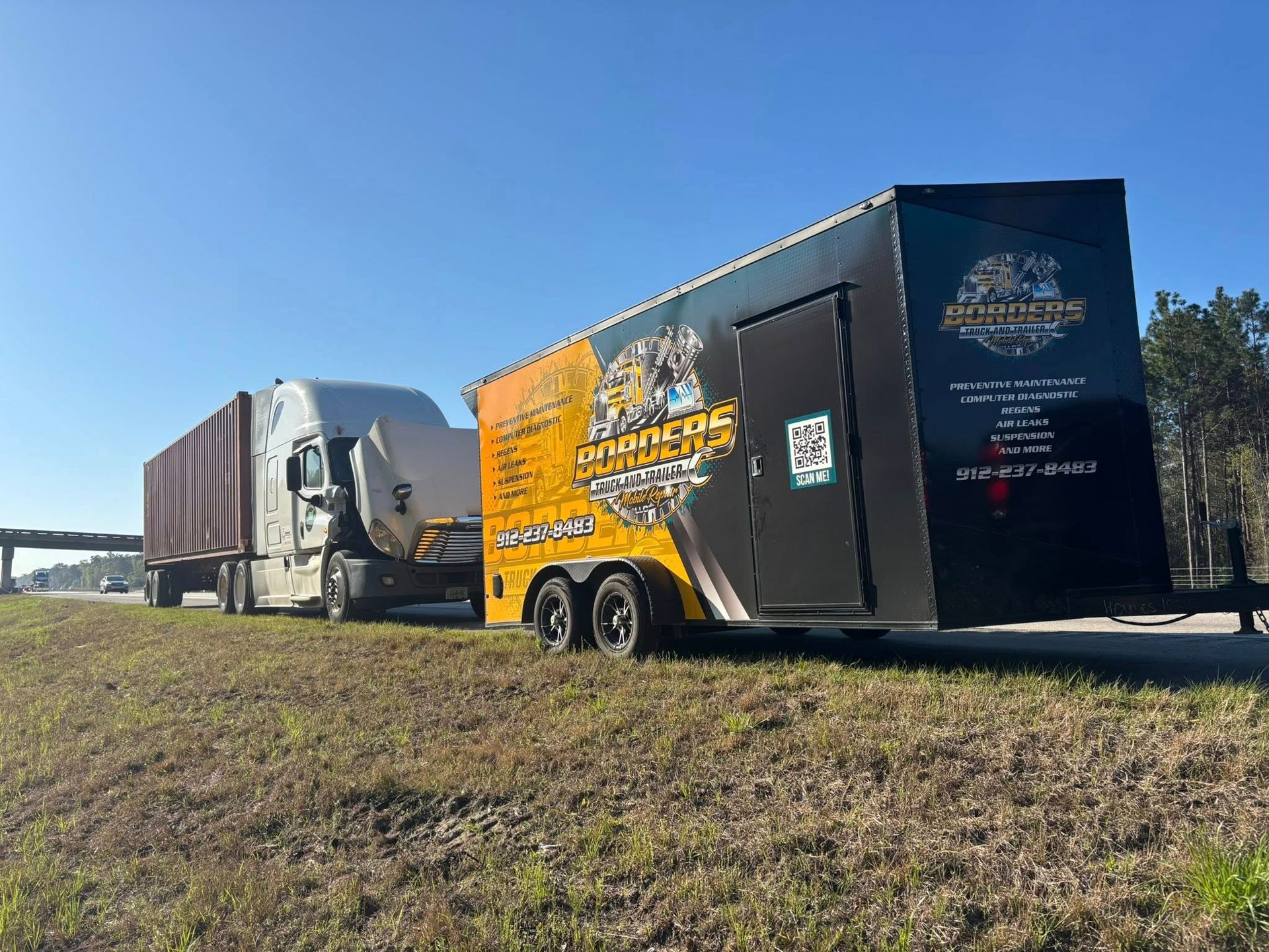 A semi-truck parked on the roadside pulling a black and yellow enclosed cargo trailer with