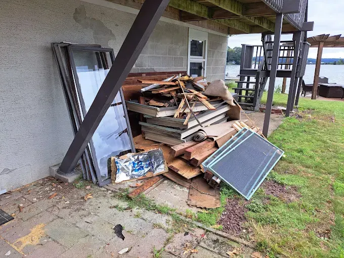 Pile of construction debris and glass windows next to a building on a grassy area, near water.