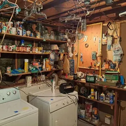 Cluttered basement with shelves of supplies, laundry machines, and a workbench.