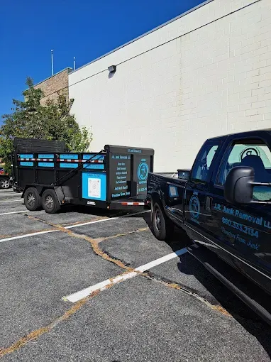Black truck pulling a trailer with black and turquoise sides parked outside a white building on a sunny day.