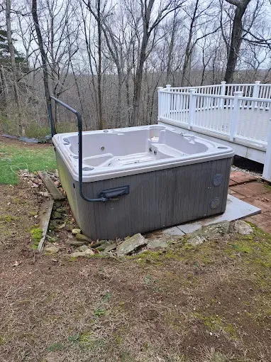 A rectangular hot tub with dark gray siding sits outdoors. A black grab bar is attached.