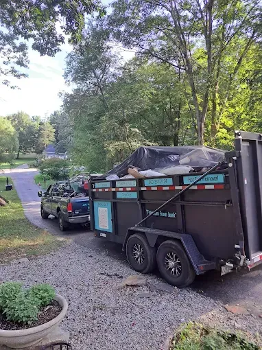 Truck pulling a loaded trailer on a driveway, trees in the background, blue accents on the trailer.