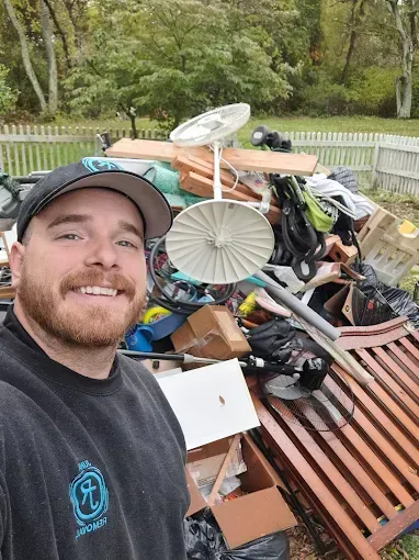 Man smiling in front of a large pile of junk in a backyard.