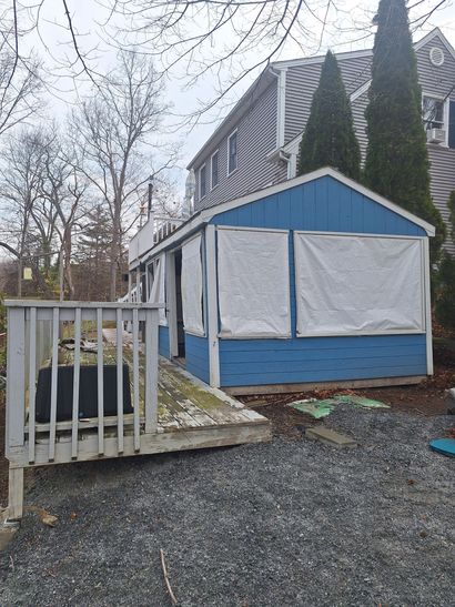 Pile of discarded items, including wood, windows, and bags, on a sidewalk in front of a house.