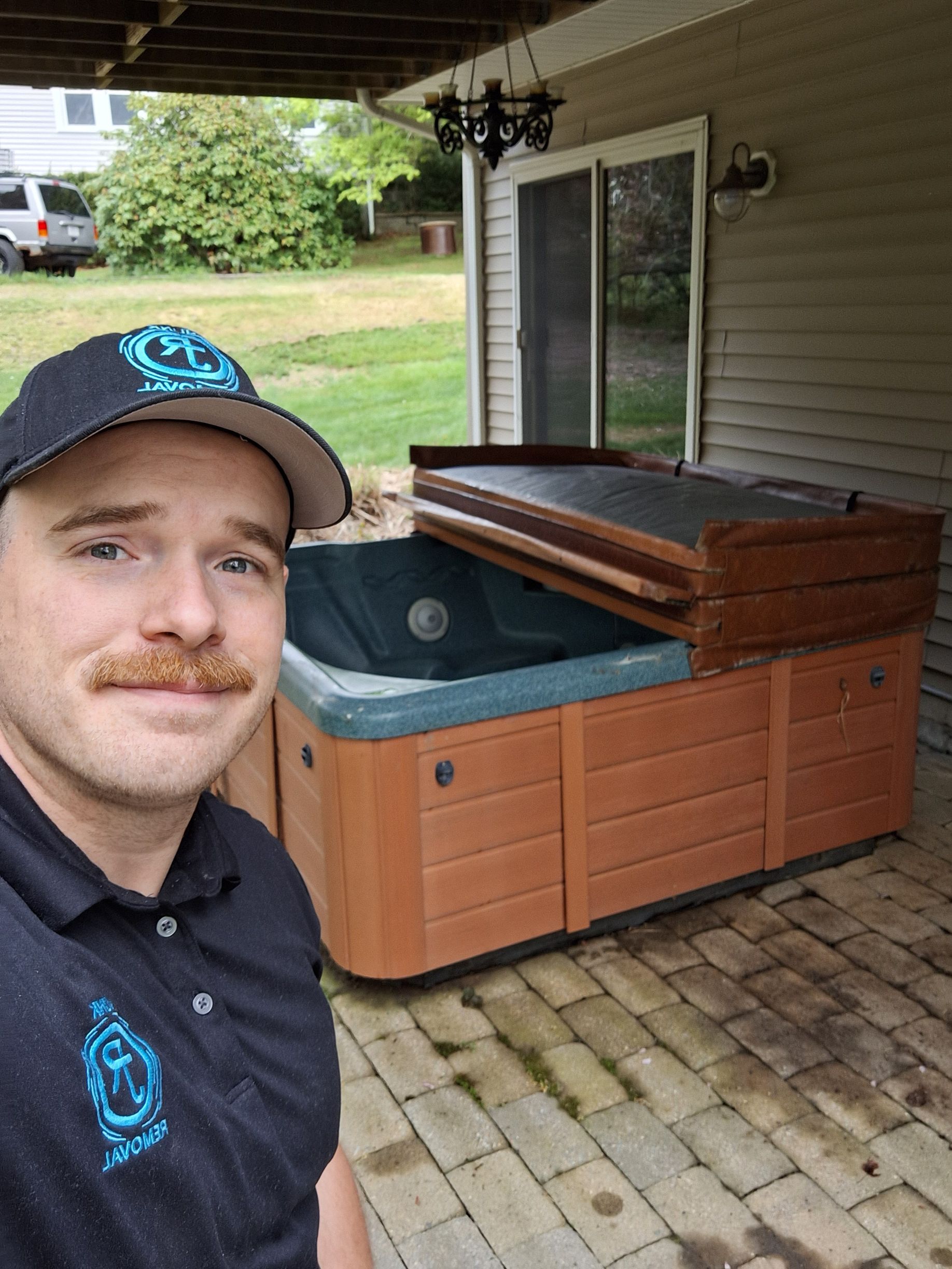 Man posing beside a covered hot tub on a brick patio under a porch roof