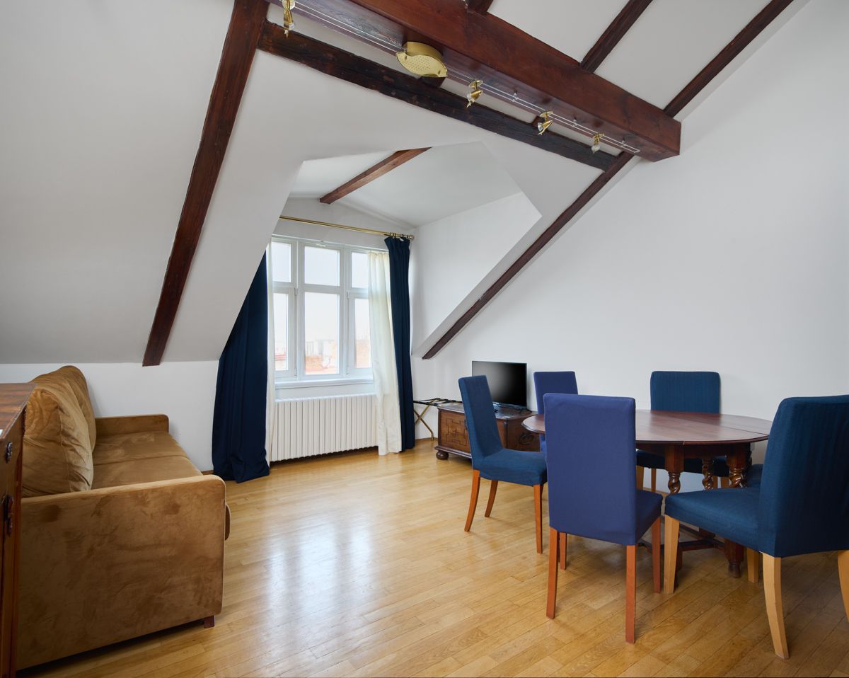 Living room with brown sofa, round table with blue chairs, and angled ceiling.