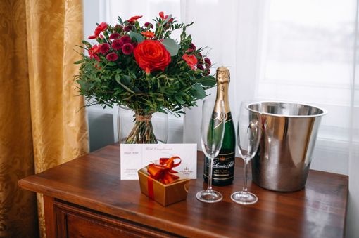 Bouquet, champagne, glasses, gift box, and ice bucket on a wooden table, near a window.