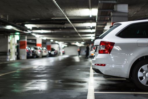 White car parked in an underground parking garage with other vehicles and two people in the background.