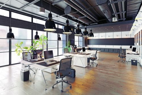 Modern open-plan office with white desks, mesh chairs, black pendant lighting, and large windows on a wooden floor.