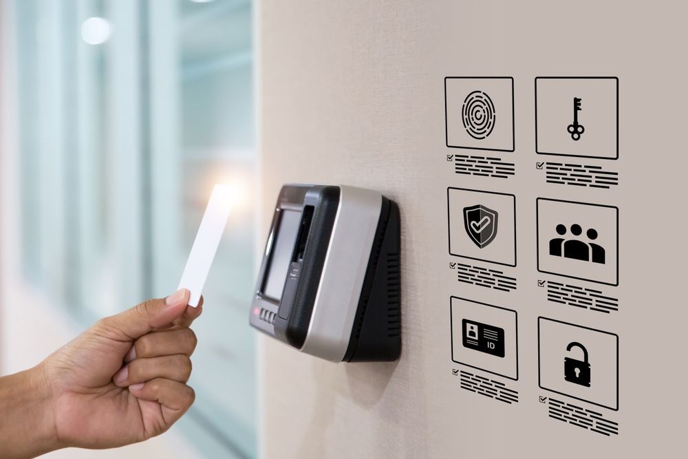 A hand holds a badge to an electronic access scanner on a wall featuring six icons for security and entry methods.