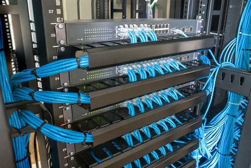 Network server rack with organized blue Ethernet cables plugged into multiple switches and patch panels.