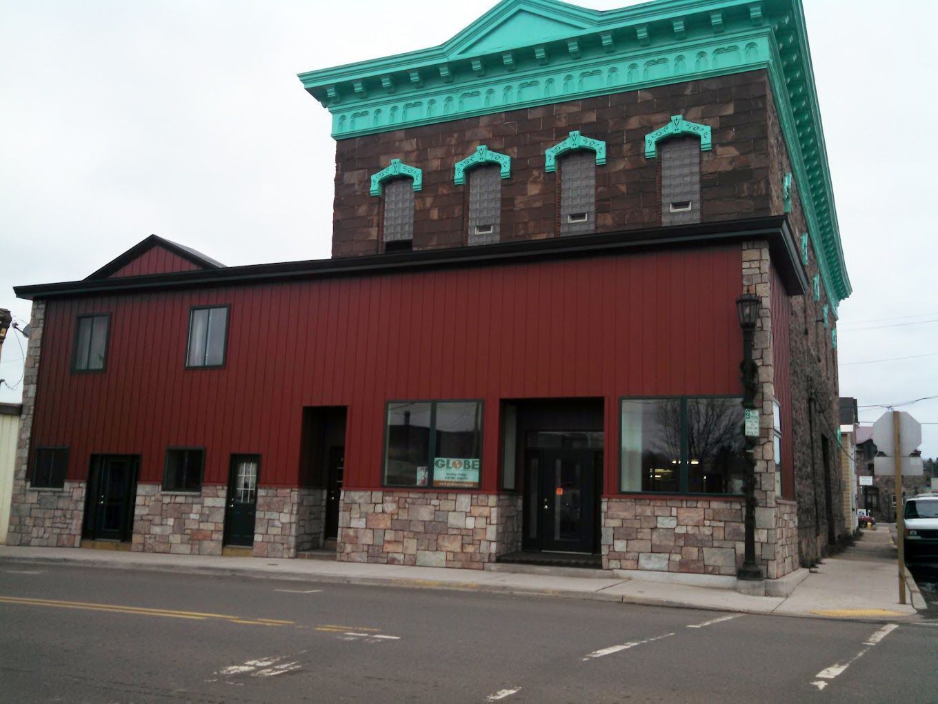 Red-walled building with stone facade; turquoise trim on the upper level, windows, and storefront.
