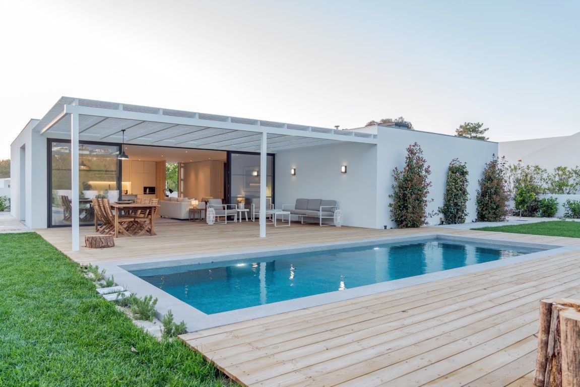 Backyard pool behind a single story white house with wooden deck