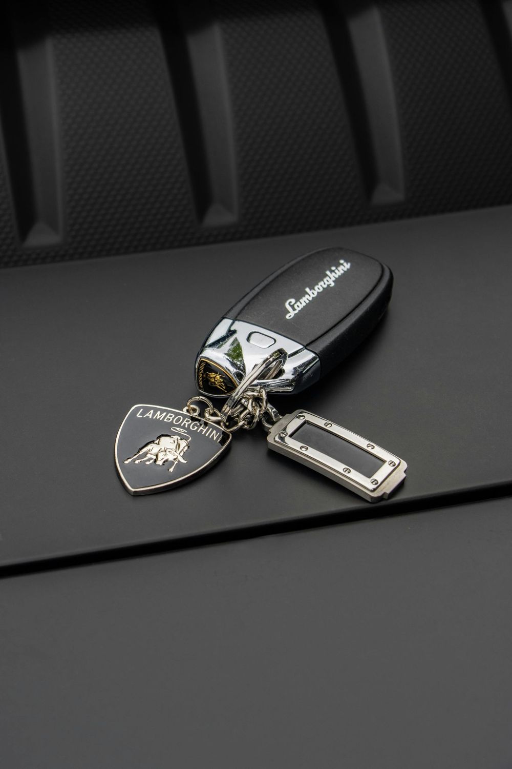 Black car key fob and keychain on a dark surface, with a silver rectangular charm.